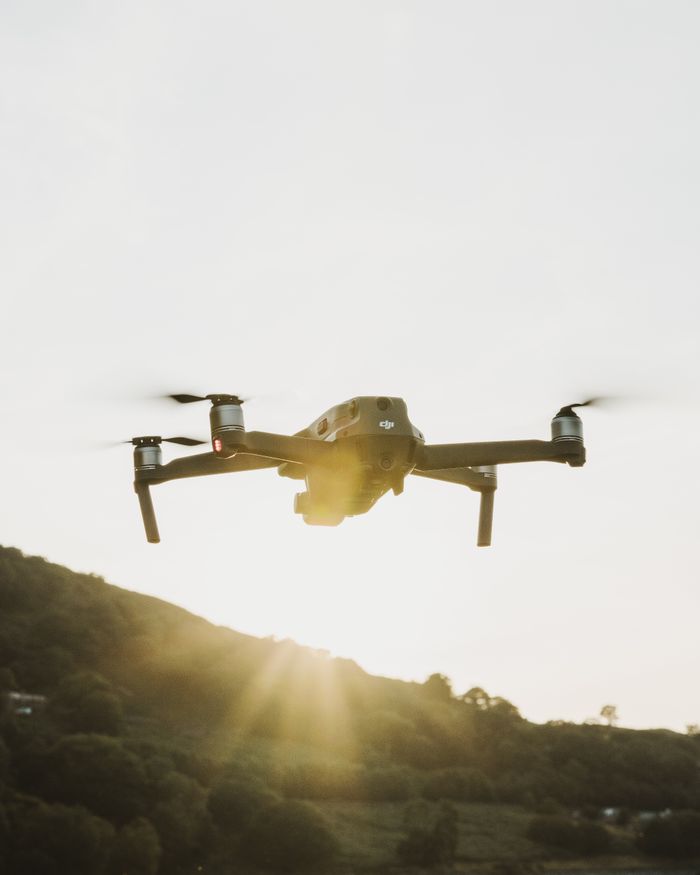 A drone flying over hilly terrain during sunrise, showcasing technology and aerial capability.
